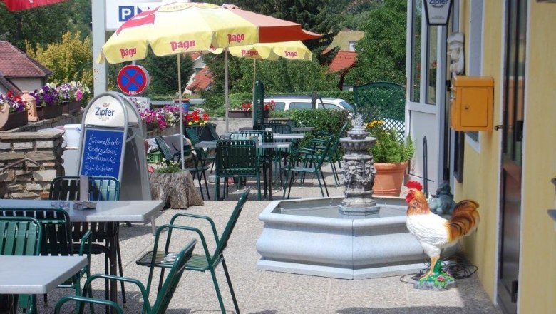 A guest garden with tables, chairs, parasols and a fountain. A rooster stands next to the fountain.