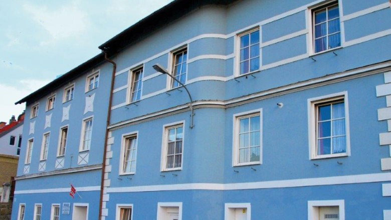 Blue façade of a multi-storey building with white window frames and doors.