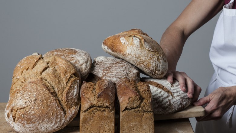 Various loaves of bread on a wooden board, held by a person in an apron.
