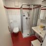 Bathroom with red tiled floor, white tiled walls, shower, washbasin and toilet.