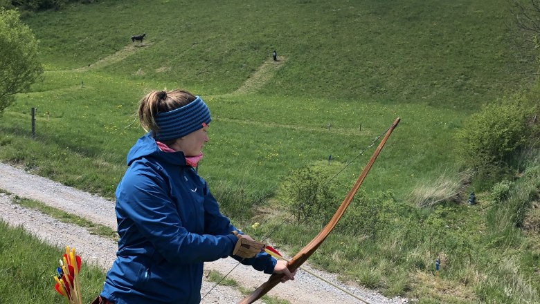 Person doing archery on a green hill under a blue sky.