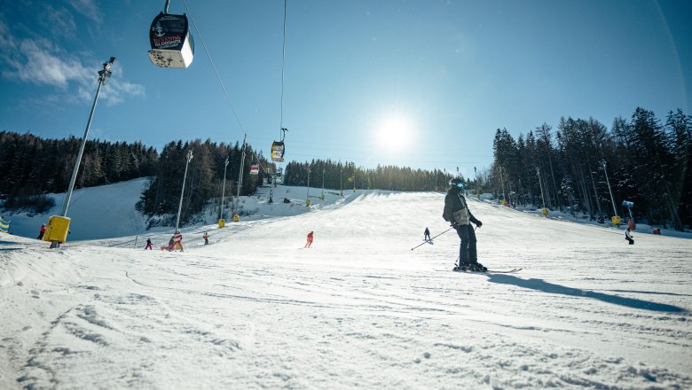 Ski slope on the Semmering Hirschenkogel with skiers and cable car in the sunshine.