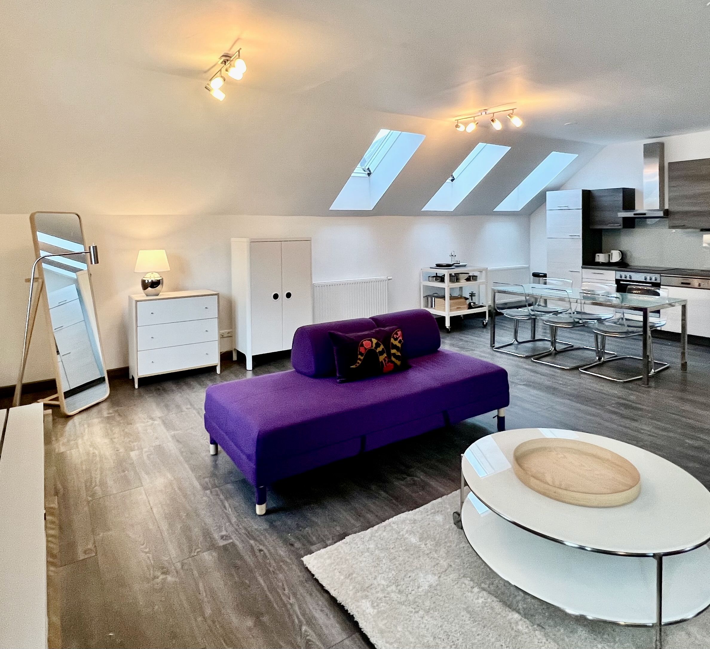 Modern loft with purple sofa, dining table and kitchen under skylights.