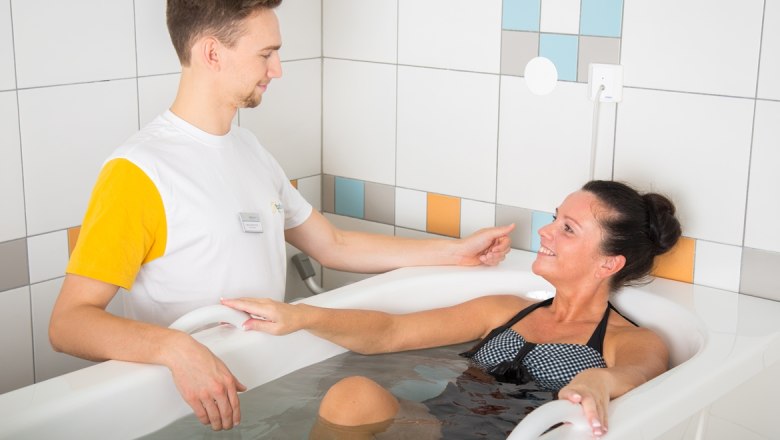A woman in a sulphur bath is cared for by a therapist.