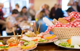 A table with traditional Austrian dishes, including cold cuts, cheese and bread in a basket with a red and white checked cloth.