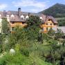 A large building with a wooden façade, surrounded by lush greenery and a mountain in the background.