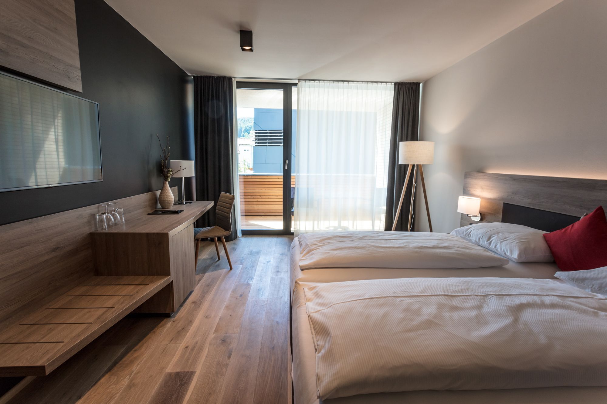 Modern hotel room with two beds, desk and balcony.