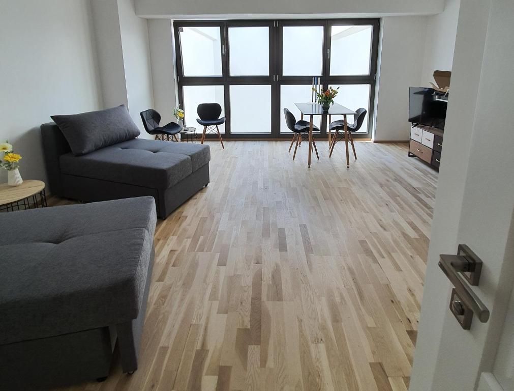 Modern room with wooden floor, gray sofas, dining table and large windows.