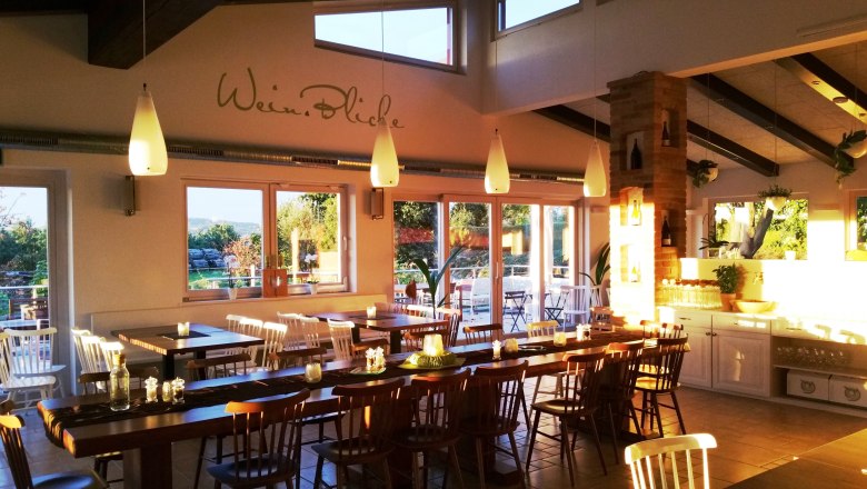 A cozy guest room with wooden tables and chairs, decorated with candles and plants, illuminated by warm sunlight.