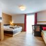 Cozy hotel room with wooden walls, double bed, single bed and red curtain.