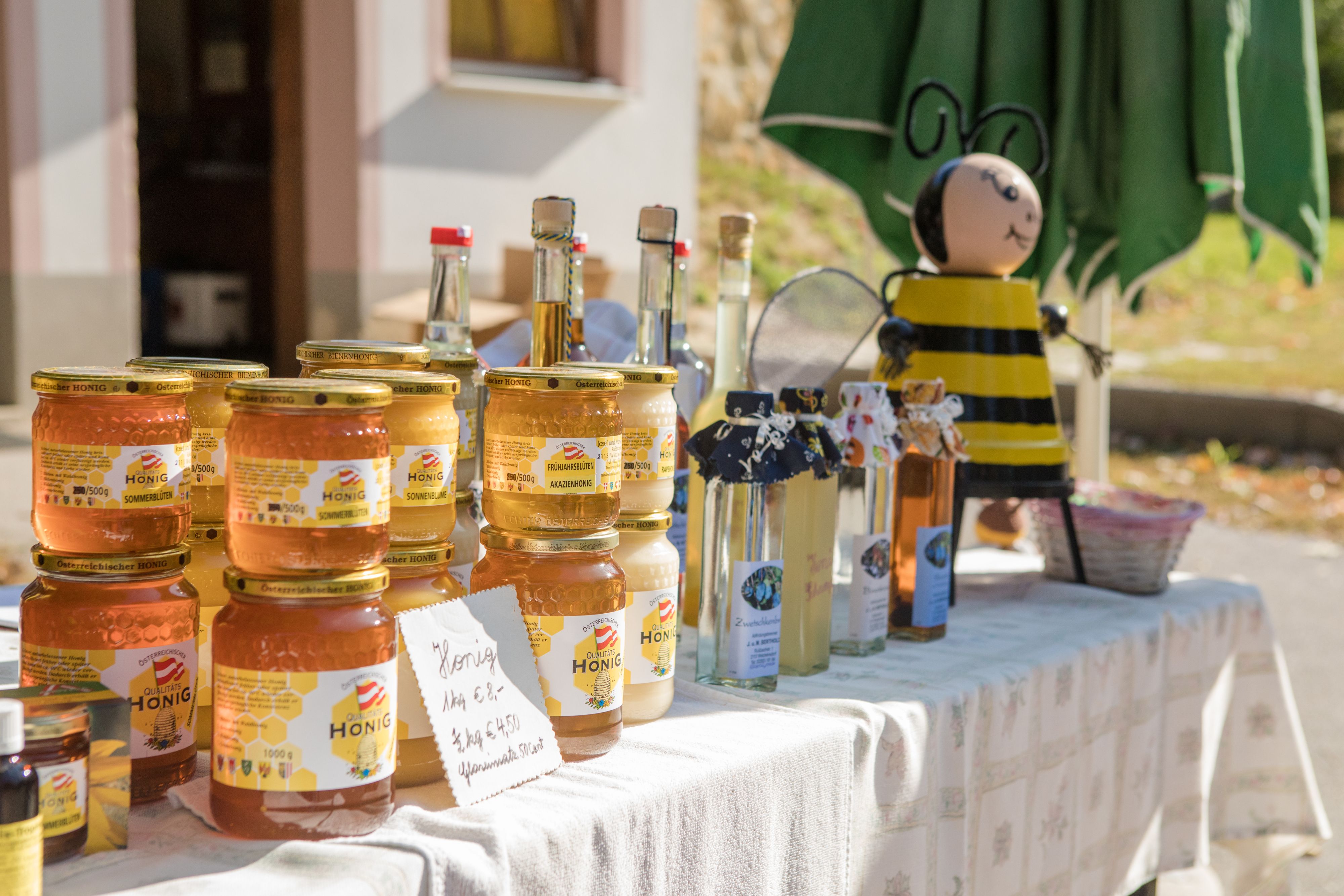 Honey jars and bottles on a table with a bee figure in the background.