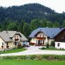 Three houses in a rural setting with a forest in the background.