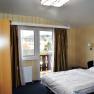 A hotel room with a double bed, window with curtains and a view of the building outside.