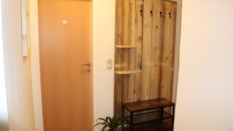 Entrance area with wooden door, wooden coat rack with hooks, bench and plant.