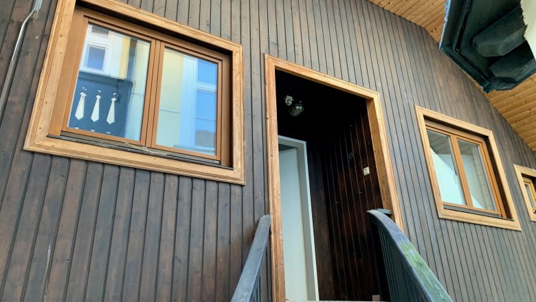 Close-up of a house facade with wooden wall and windows.