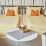 Cozy double room with two single beds, yellow bed linen and orange pillows. A round table with a flower arrangement stands between two armchairs.