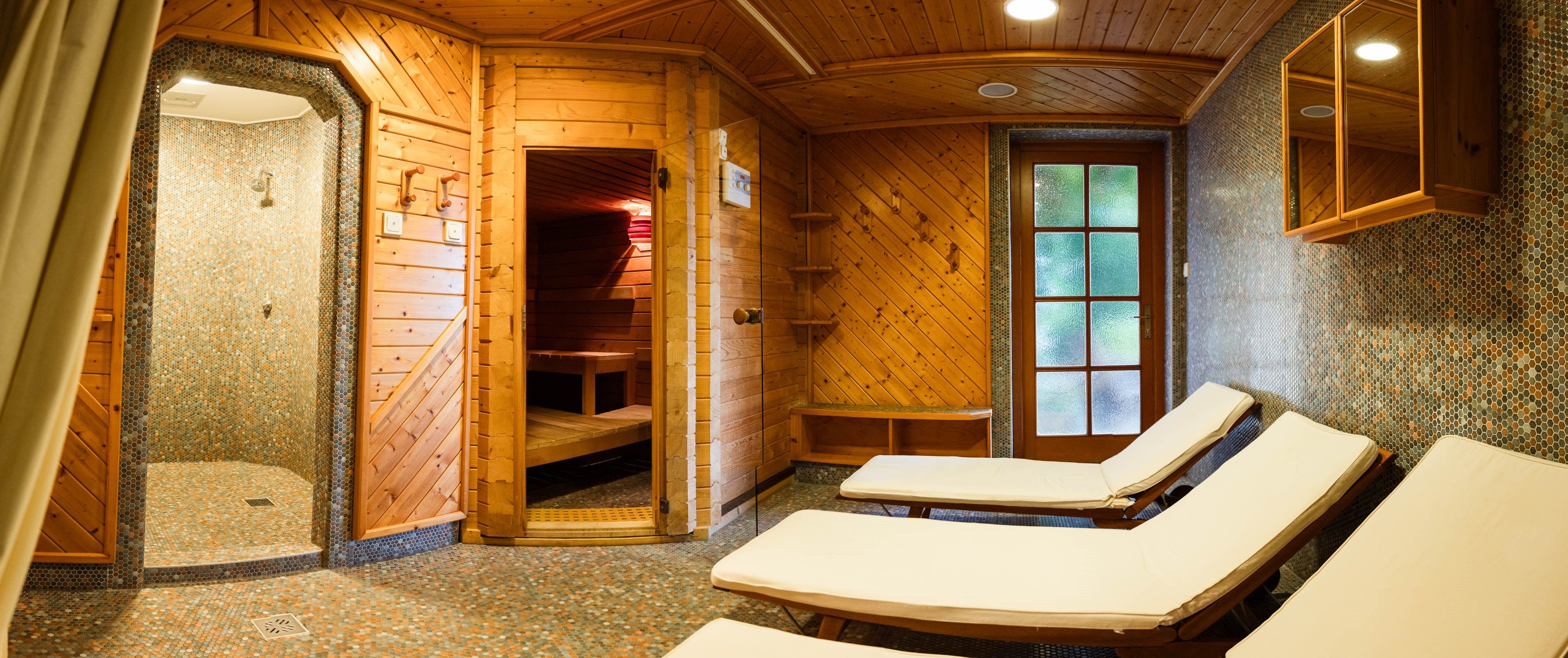 A cozy sauna area with wooden panelling, loungers and a shower.