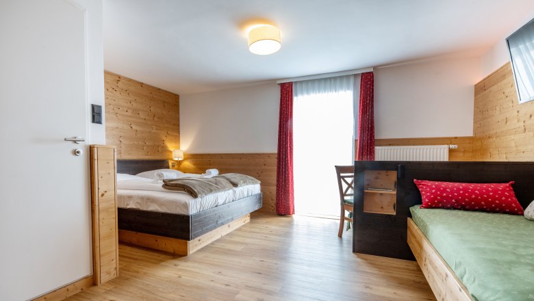 Cozy hotel room with wooden walls, double bed, single bed and red curtain.