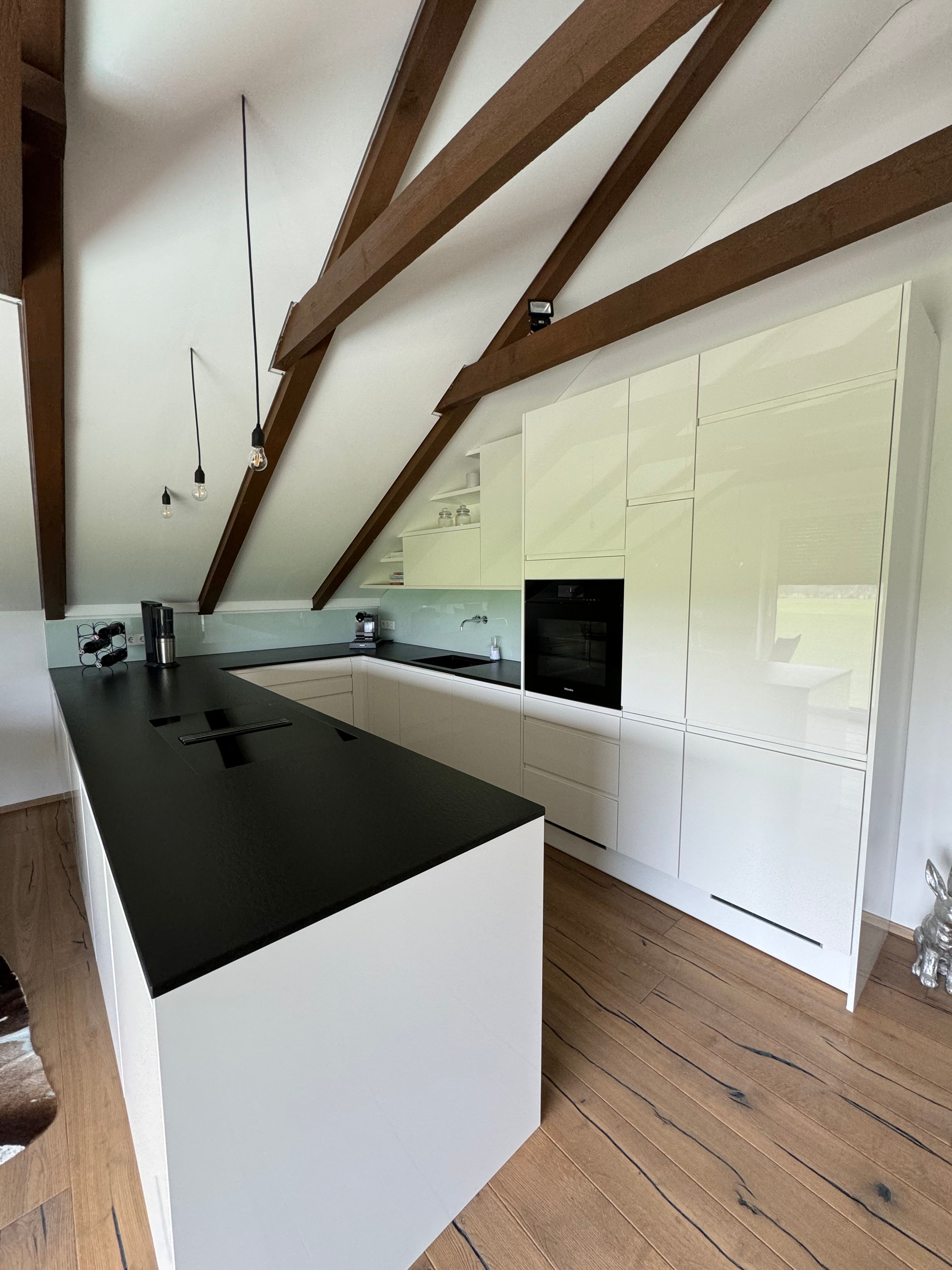 Modern kitchen with white cupboards, black worktop and wooden beams on the ceiling.