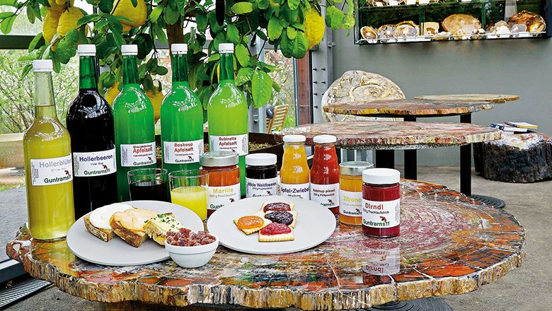 Various bottles and jars of drinks and jams on a table made of petrified wood.