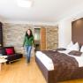Modern furnished hotel room with double bed, stone wall and woman in green blazer.