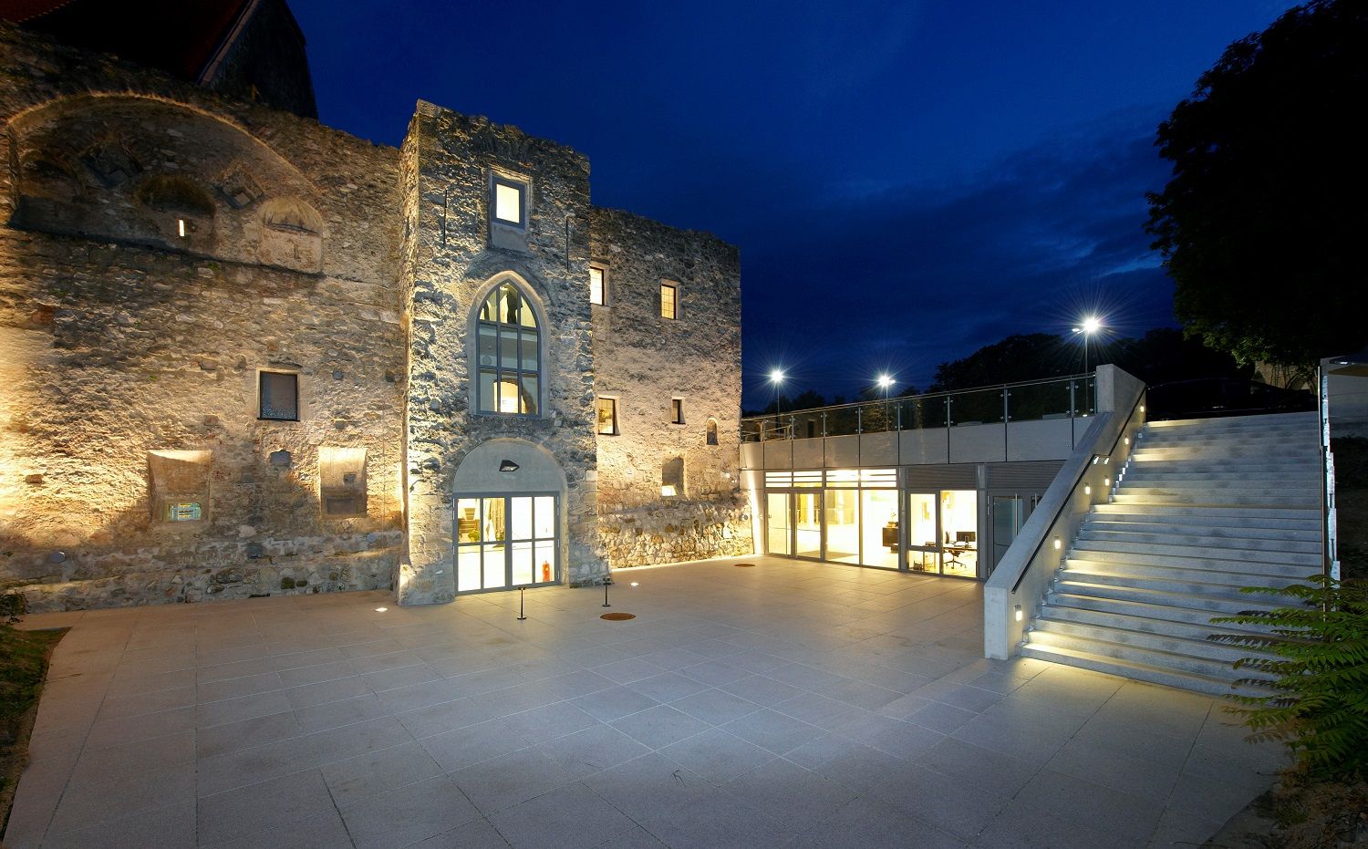 Illuminated BURG Perchtoldsdorf at night with modern extension and staircase.