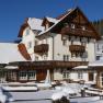 A large, traditional house in the snow with wooden decorations and blue sky in the background.