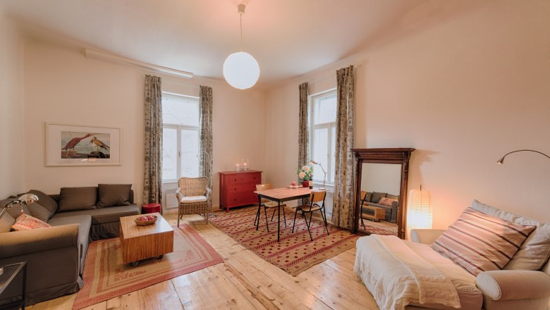 Cozy living room with wooden floor, sofa, armchair, dining table and large mirror.