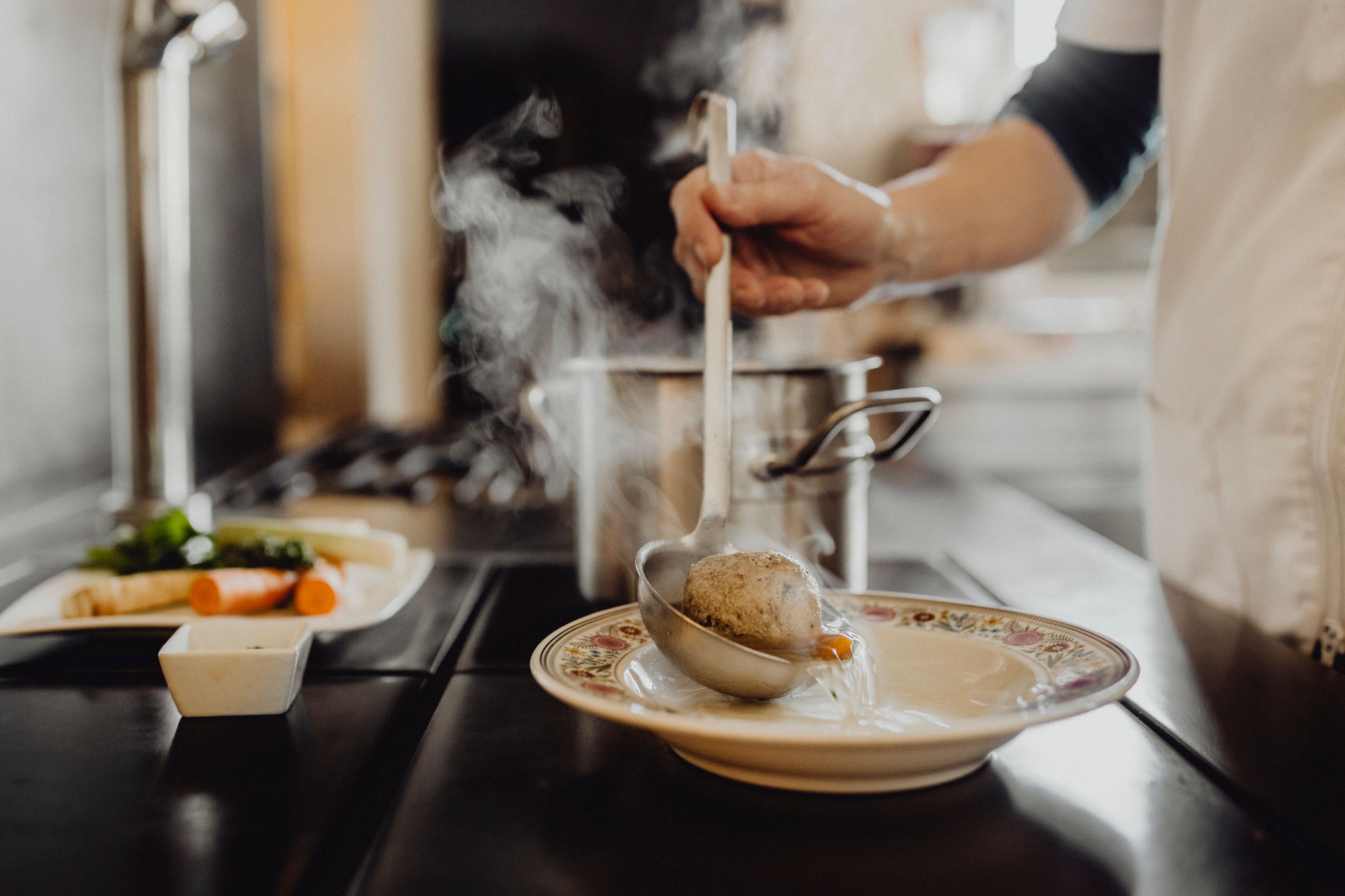 One person ladles soup with a dumpling from a pot into a plate.