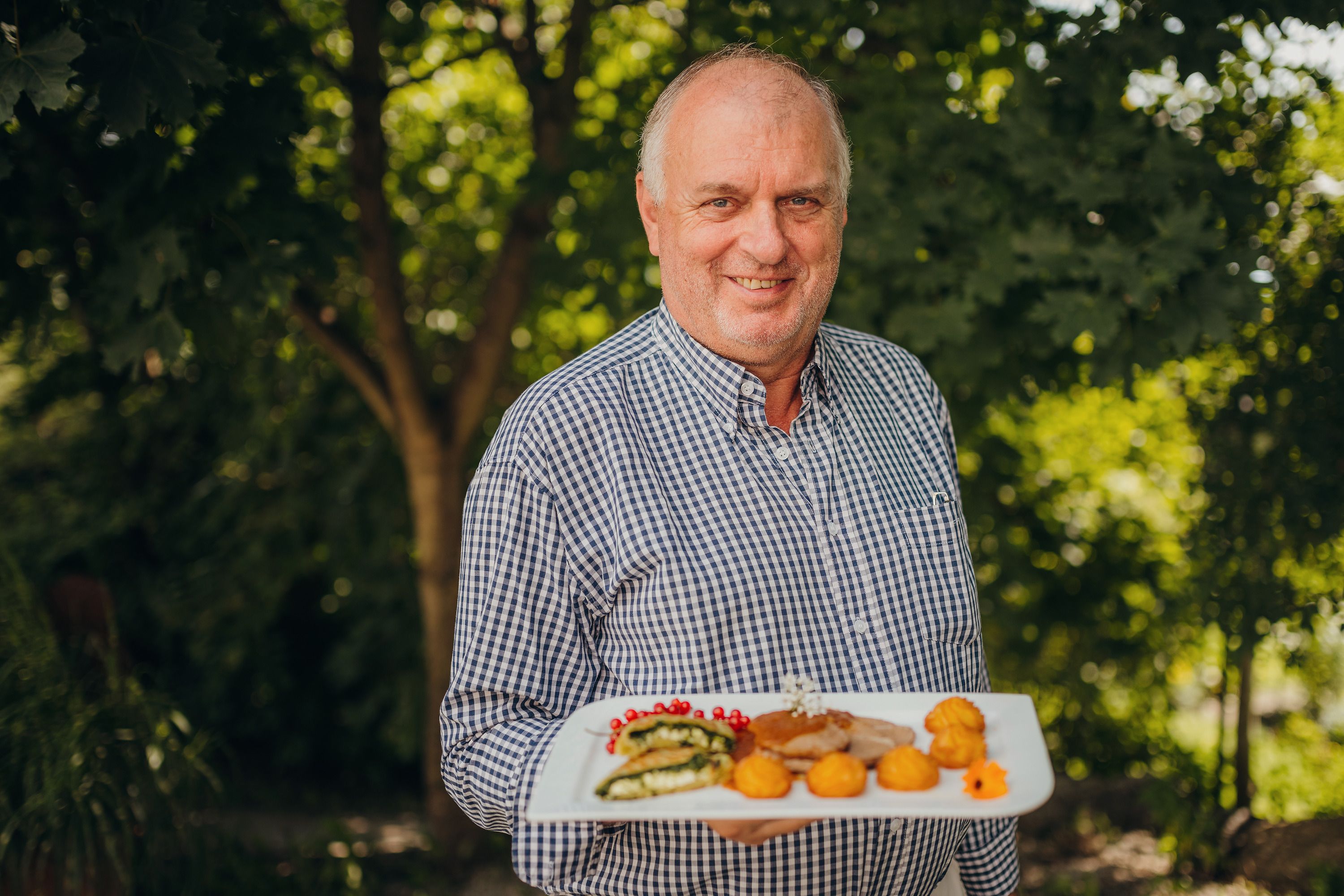 A man in a checkered shirt holds a plate with decoratively arranged food outside.