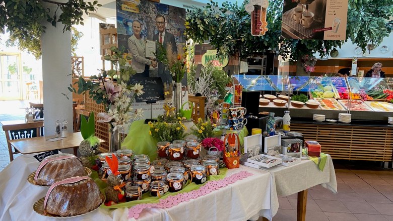 A table with jam jars, cakes and decorations in a restaurant with a buffet in the background.