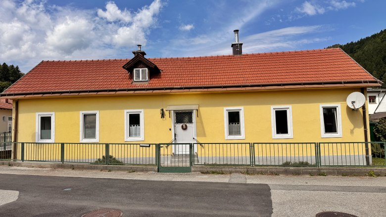 House view, © Christoph Menhofer Yellow house with a red roof and several windows, surrounded by a green fence.