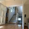 Interior view of a living room with wooden floor, stairs and open doors.