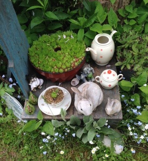Garden arrangement with teapot, cup, rabbit figurines and succulents.