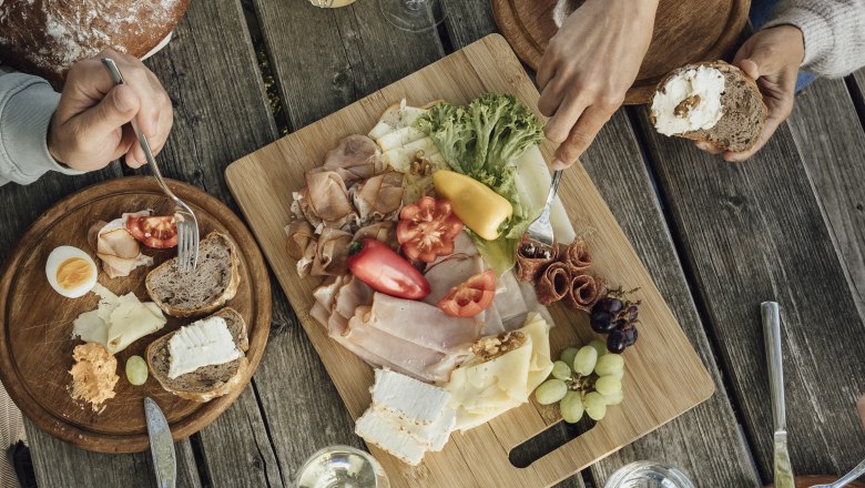 A rustic wooden table with a snack of bread, cheese, sausage, vegetables and wine.