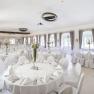 Elegant ballroom with white tables and chairs, decorated with candlesticks and flowers.