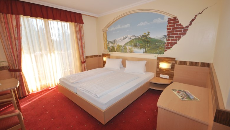Double room with double bed, wall painting and red carpet.