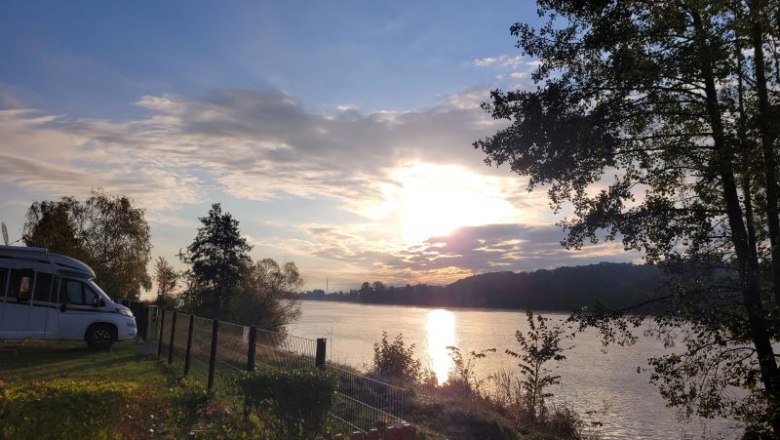 Sunset over a river with motorhome and trees in the foreground.
