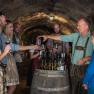 A group of people in traditional dress at a wine tasting in a wine cellar.