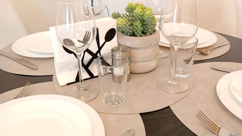 A laid table with plates, glasses, cutlery and a small plant in the middle.