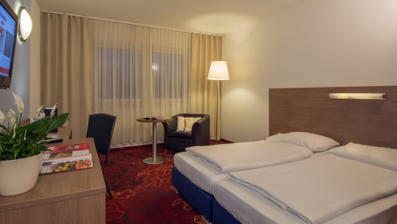 Double room with red carpeted floor, desk and large double bed.