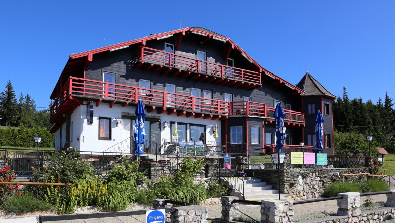 A large, traditional house with red wood and white walls, surrounded by a garden and blue parasols.