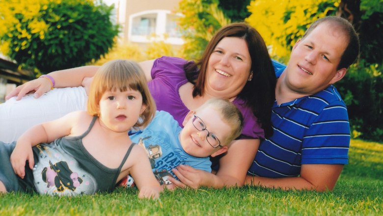 A family lies smiling on a meadow, consisting of two adults and two children.