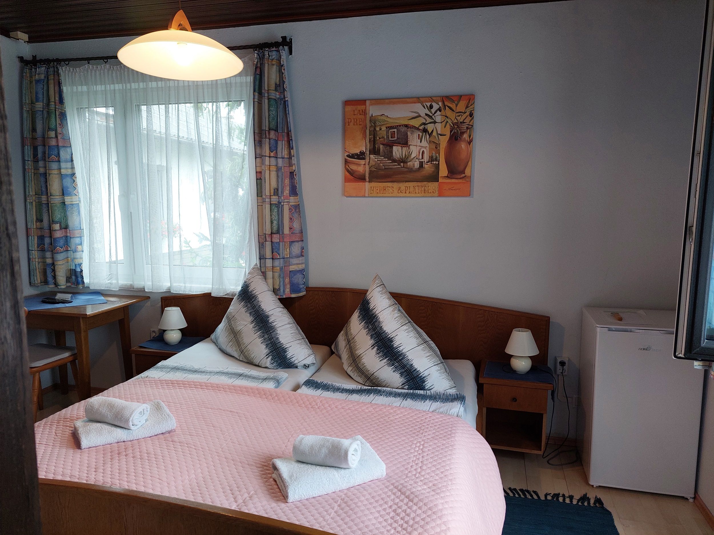 Comfortable hotel room with double bed, bedside lamps, small fridge and window with curtains.