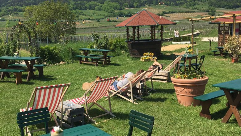 Garden with sun loungers and tables, hills and blue sky in the background.
