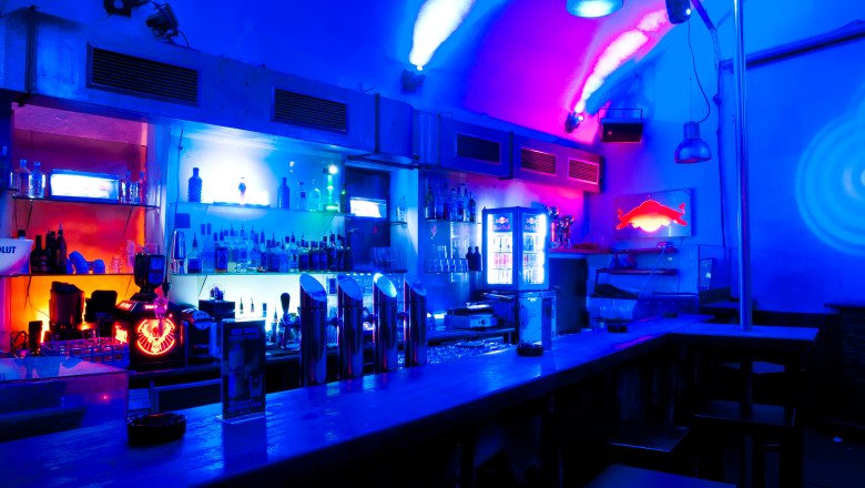 Bar with blue and red lighting, bottles and glasses on the shelf.