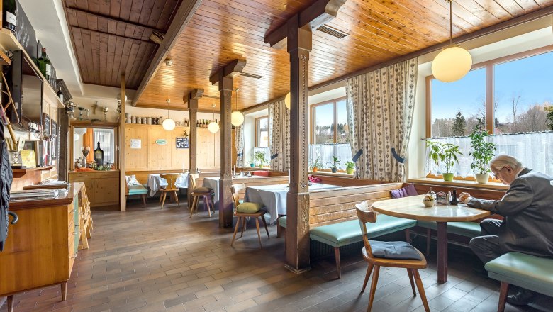 Cozy dining room with wooden furniture and large windows, a man is sitting at a table.