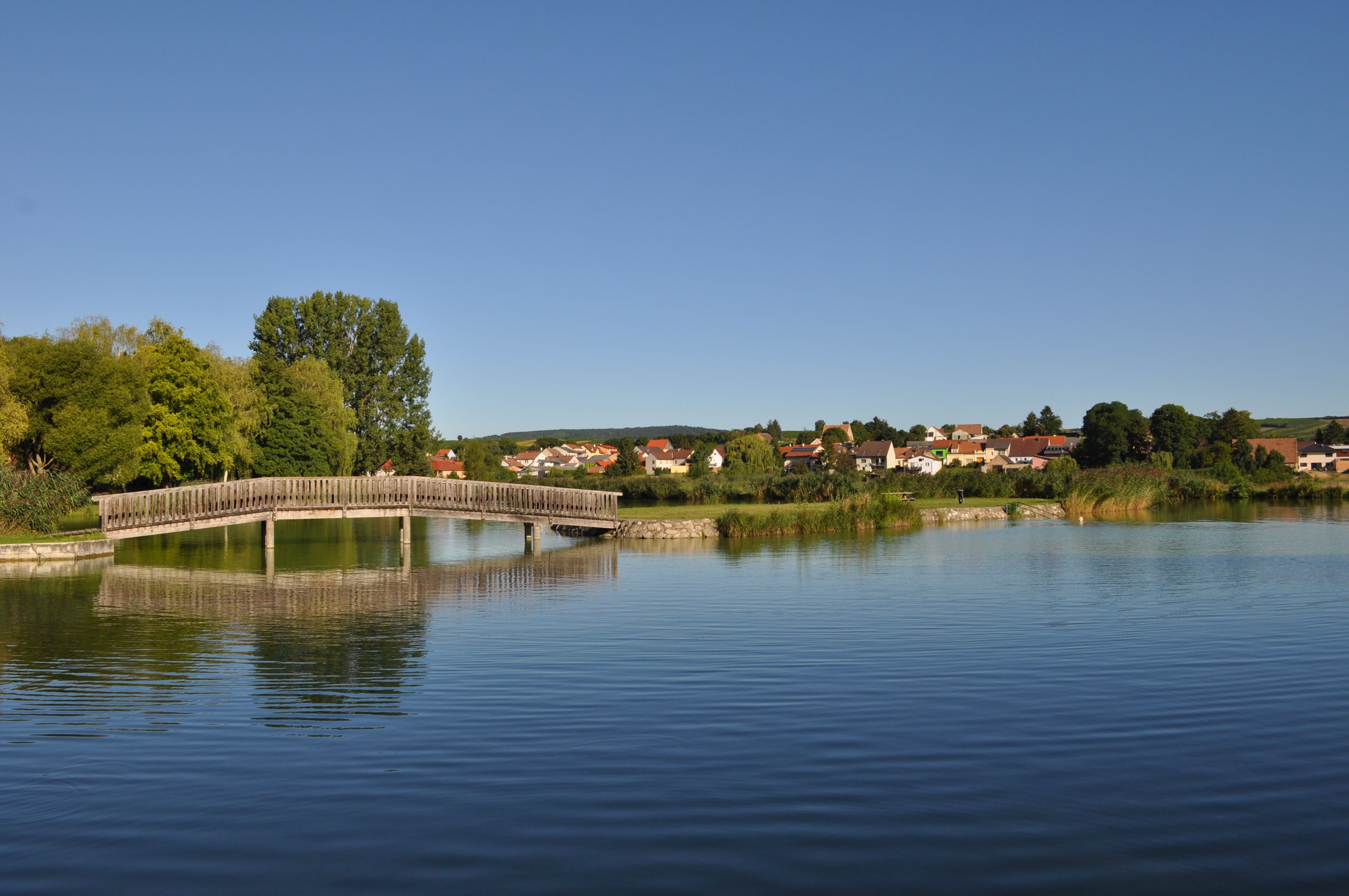 Wooden bridge over a quiet pond with a village in the background.