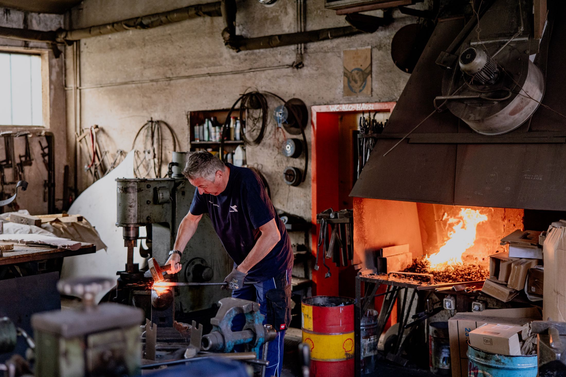 A blacksmith works in a workshop with a burning forge fire.
