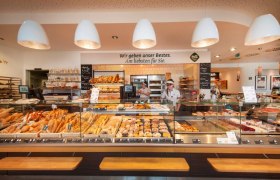 Interior view of a bakery with a counter full of baked goods and two employees.